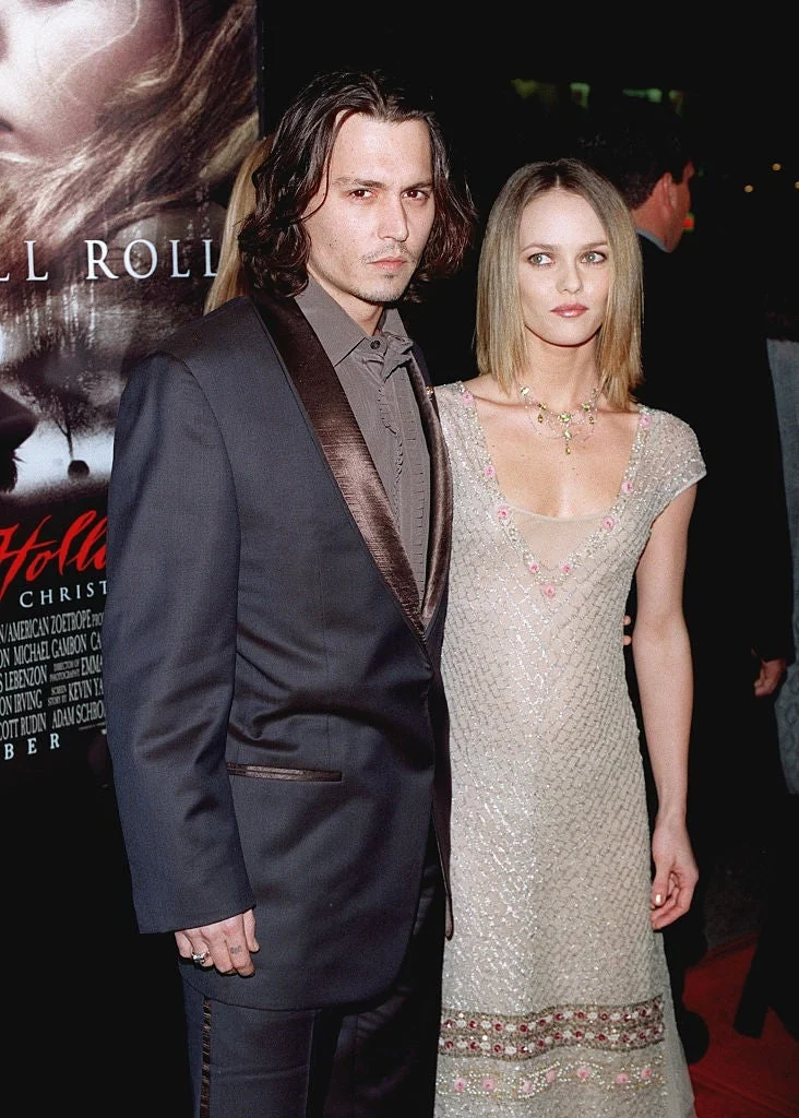 A man in a dark suit with satin lapels and a woman in a beaded gown pose together at a formal event