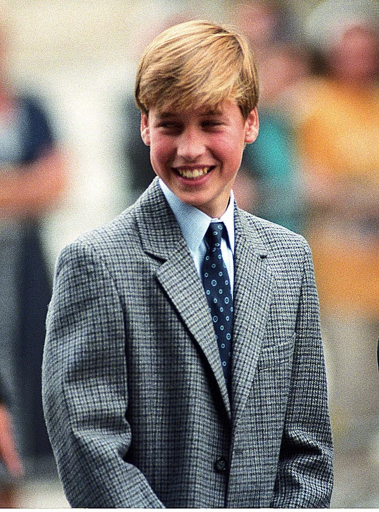 A young man in a suit with a checkered blazer and polka dot tie smiles at an outdoor event