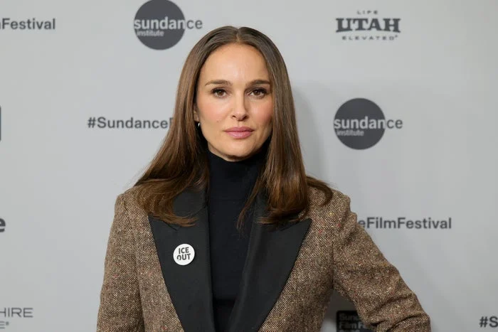 A woman on the red carpet in a tailored blazer with a "Time's Up" pin, looking poised at Sundance Film Festival backdrop