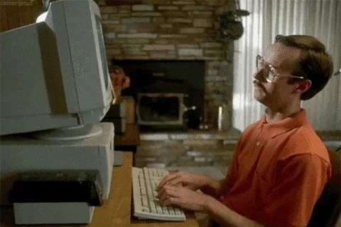 Person in front of an old computer, typing attentively. Retro home setting with a brick fireplace in the background