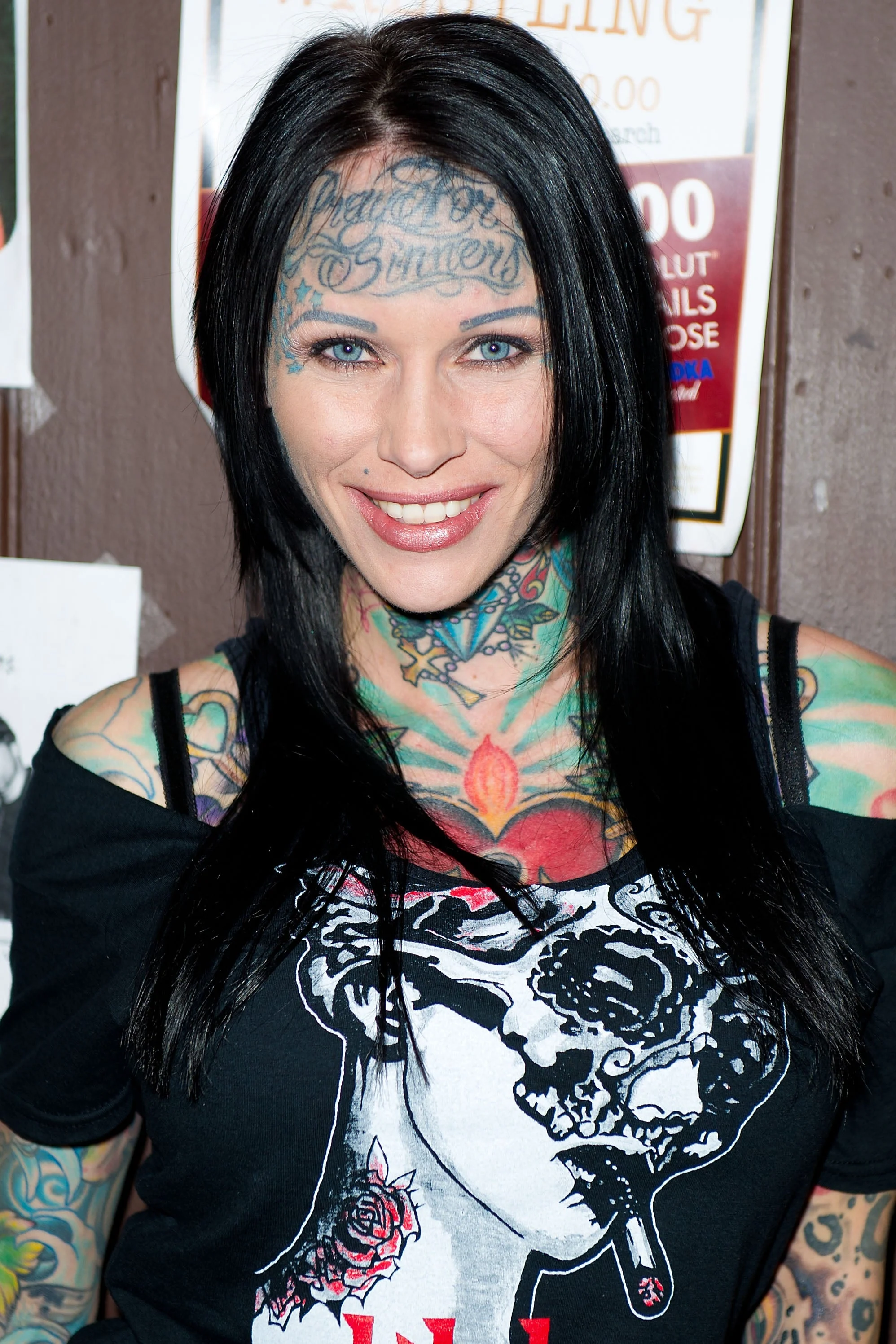 Person with extensive tattoos, including face and neck, wearing a black top with a graphic design