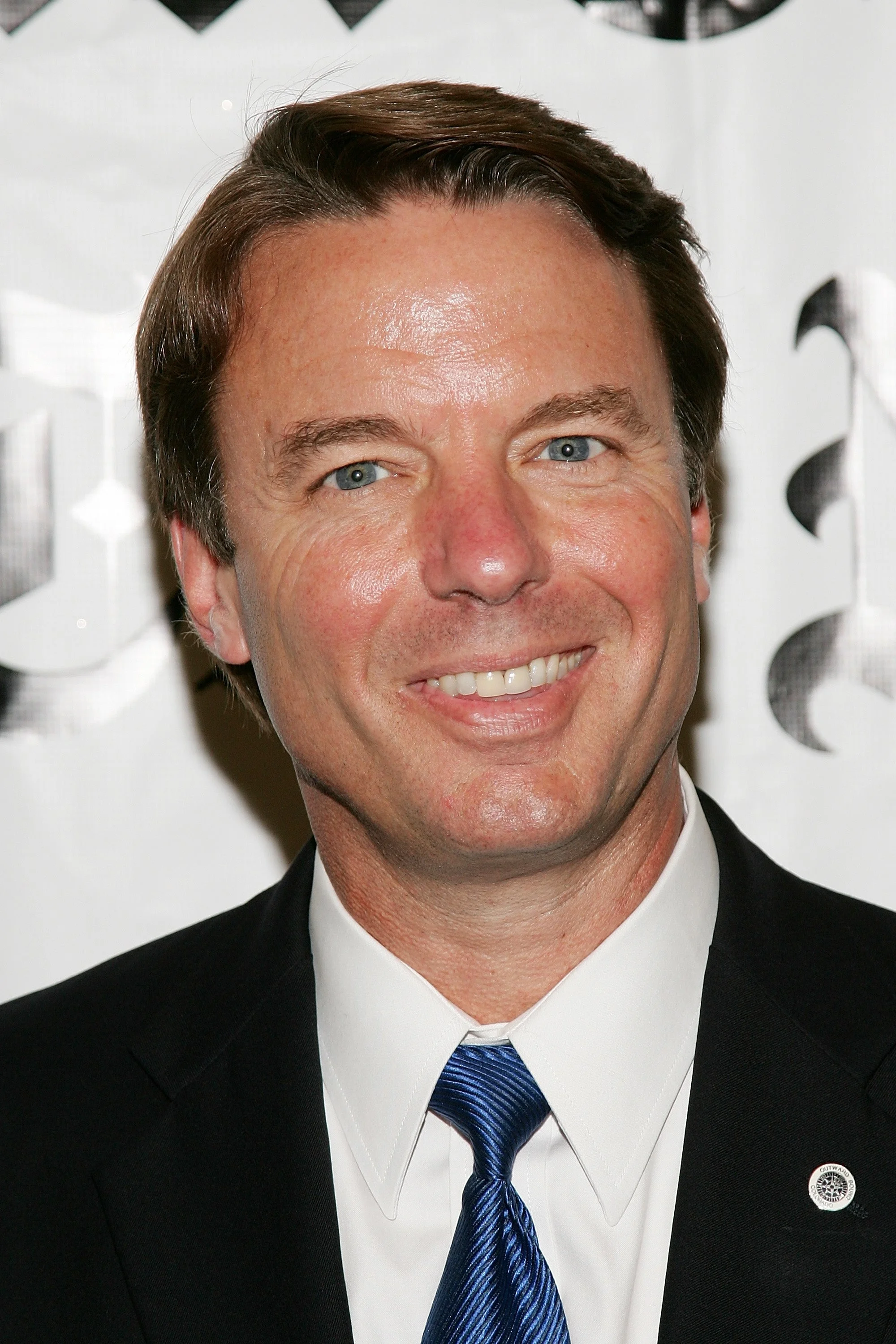 The person is wearing a suit and tie, smiling at an event