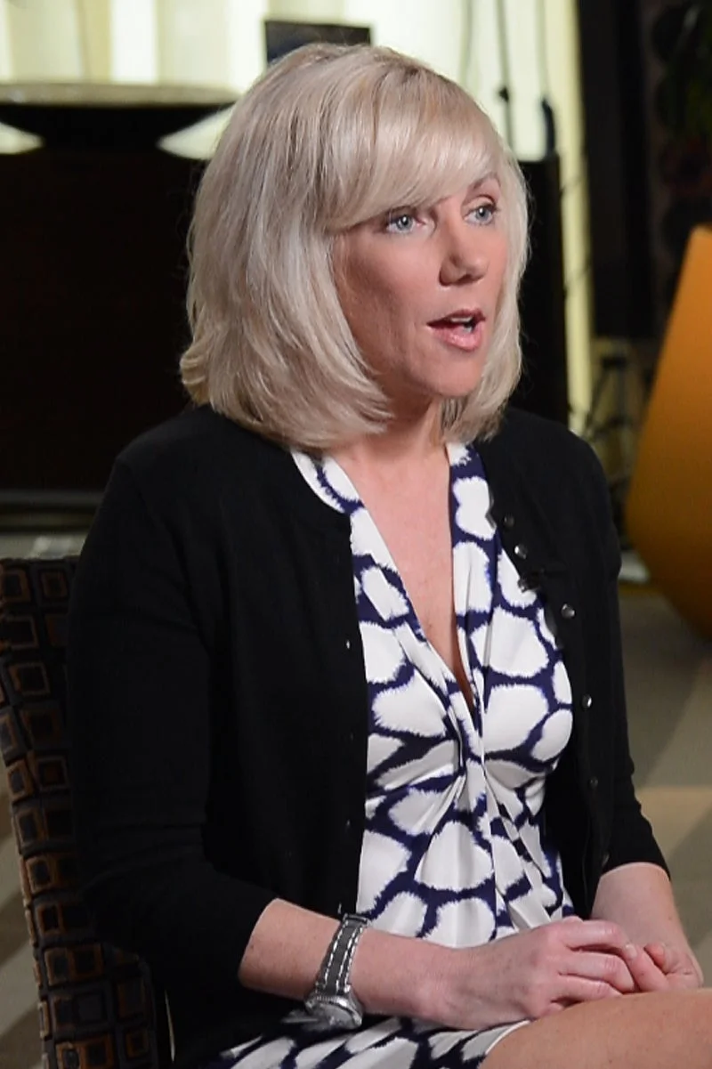 Two people seated and talking in an interview setting; one holds papers, suggesting a discussion or interview taking place