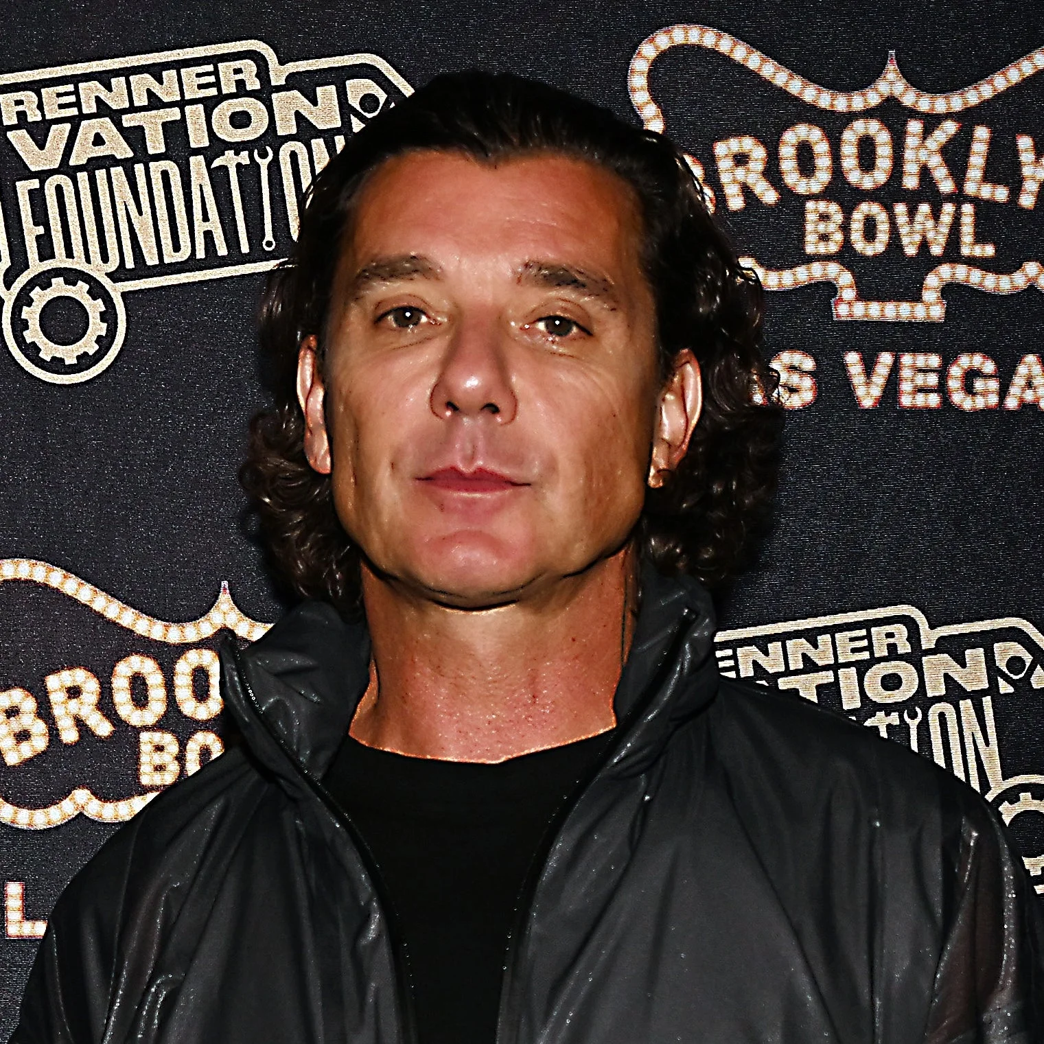 Person in casual dark jacket and pants stands against a step-and-repeat backdrop featuring "Brooklyn Bowl" and "Las Vegas" logos