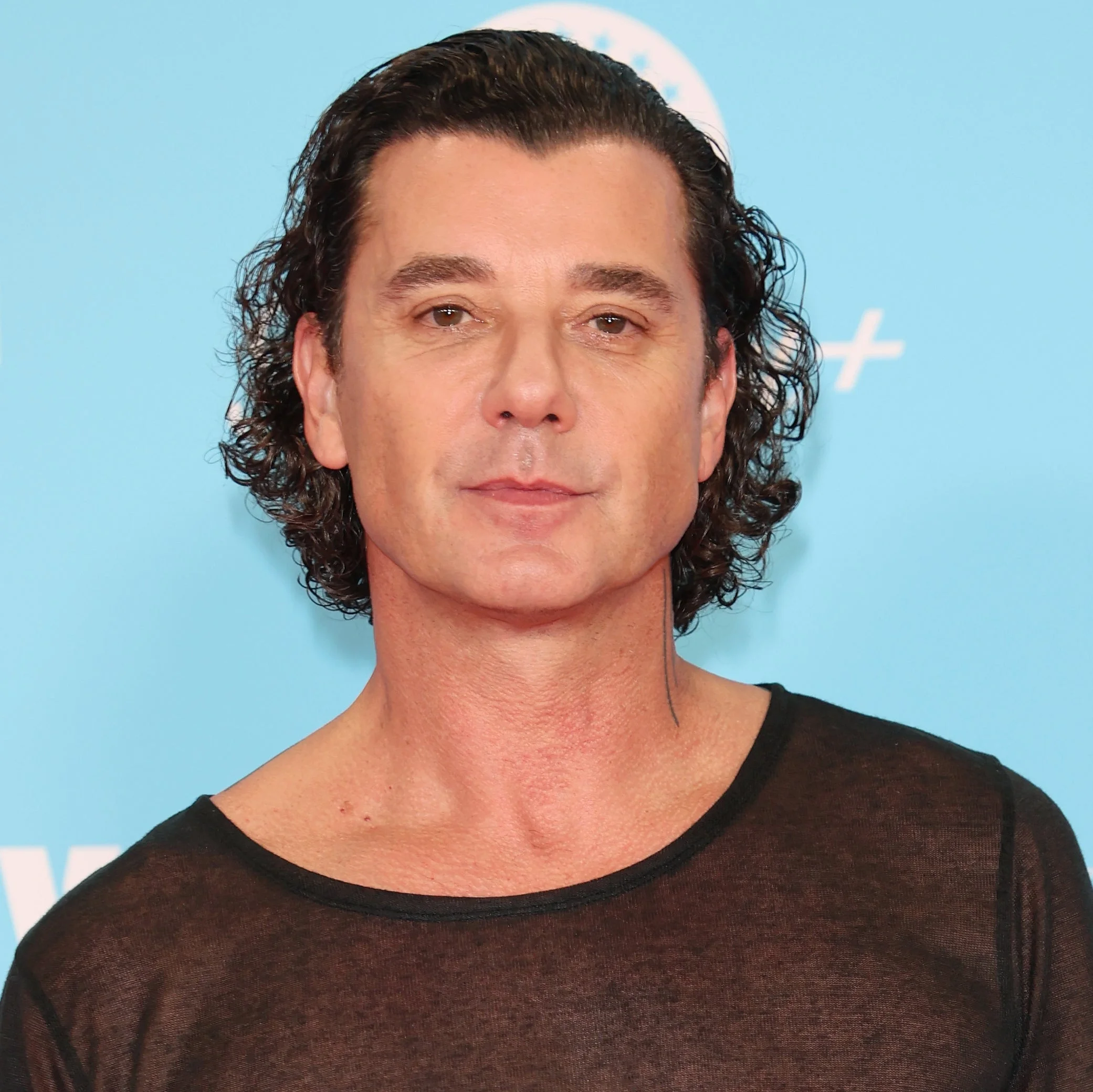 A person on the red carpet at the MTV EMA 2024 in a sheer black t-shirt and black pants, showing arm tattoos