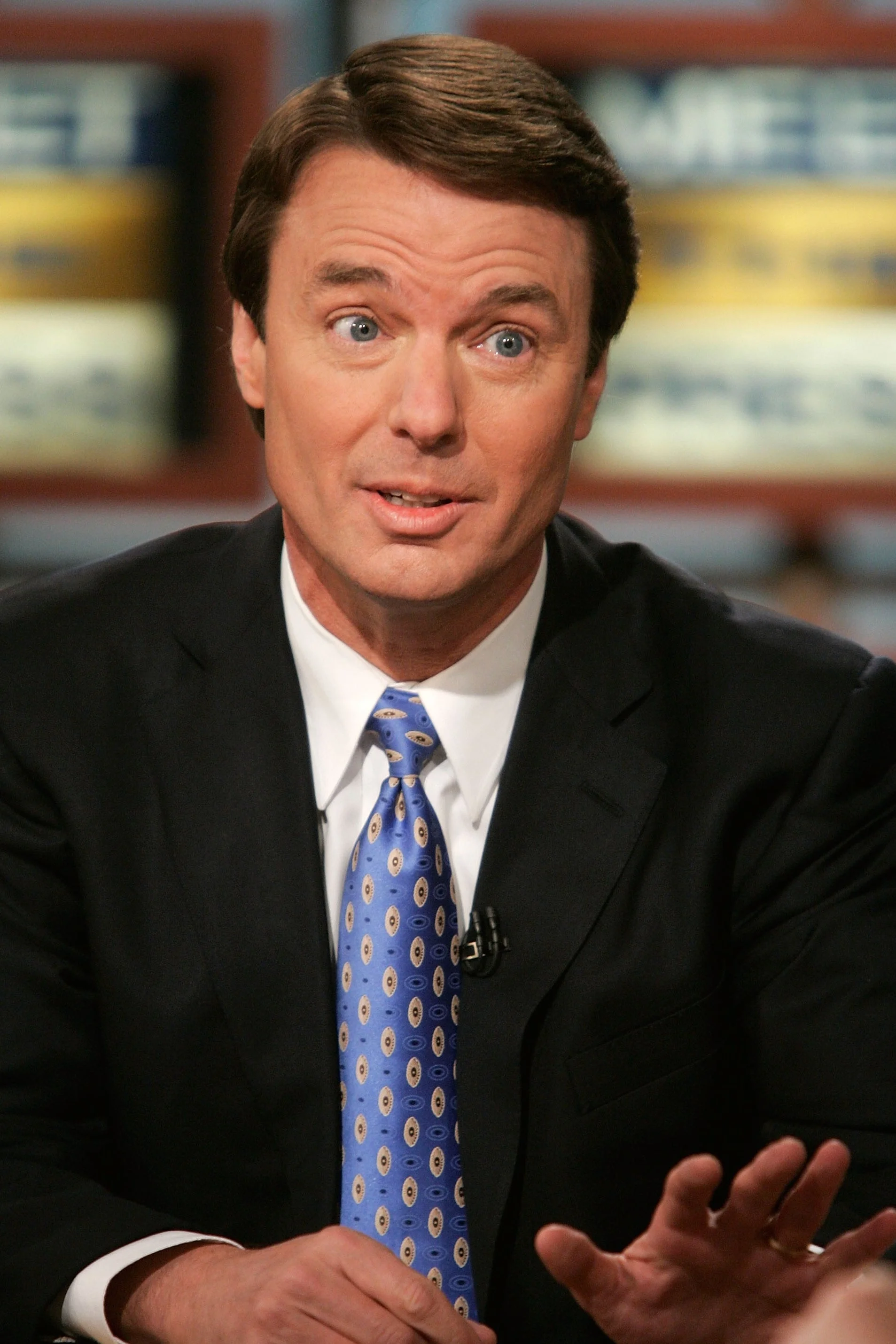 Person in a suit and patterned tie speaking during a television interview