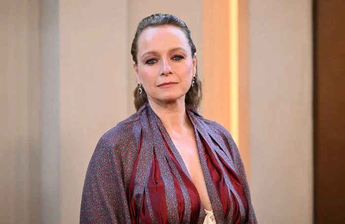 A person in a patterned dress with a plunging neckline poses indoors. The style is elegant and contemporary