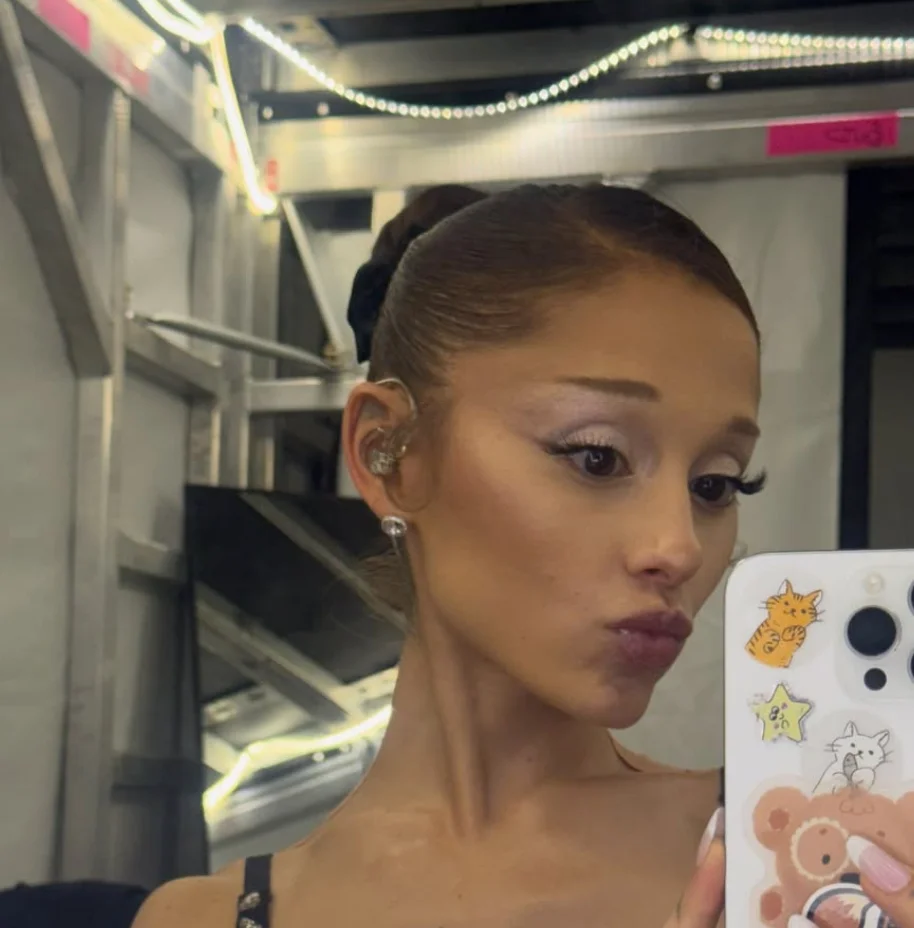 Person taking a selfie in a backstage setting, wearing an earpiece and posing with a playful expression