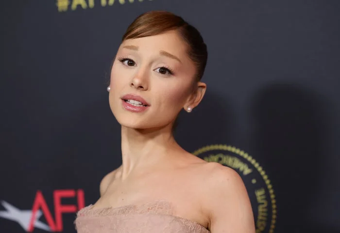 Person on a red carpet in an elegant, strapless dress with sleek hairstyle, posing in front of event logos
