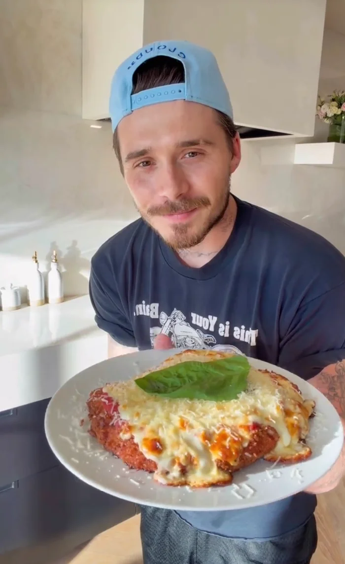 Brooklyn Beckham holding a plate of a cheesy baked dish