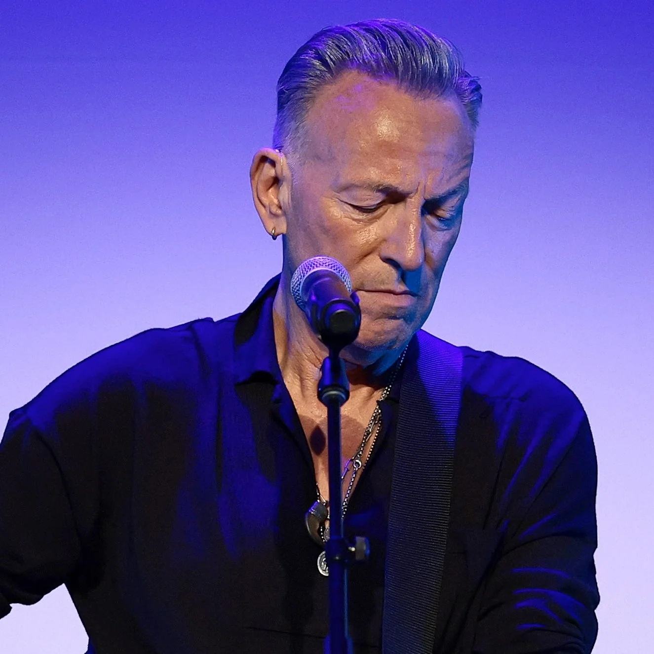 Bruce Springsteen performs on stage with an acoustic guitar, wearing a black shirt, focused on playing