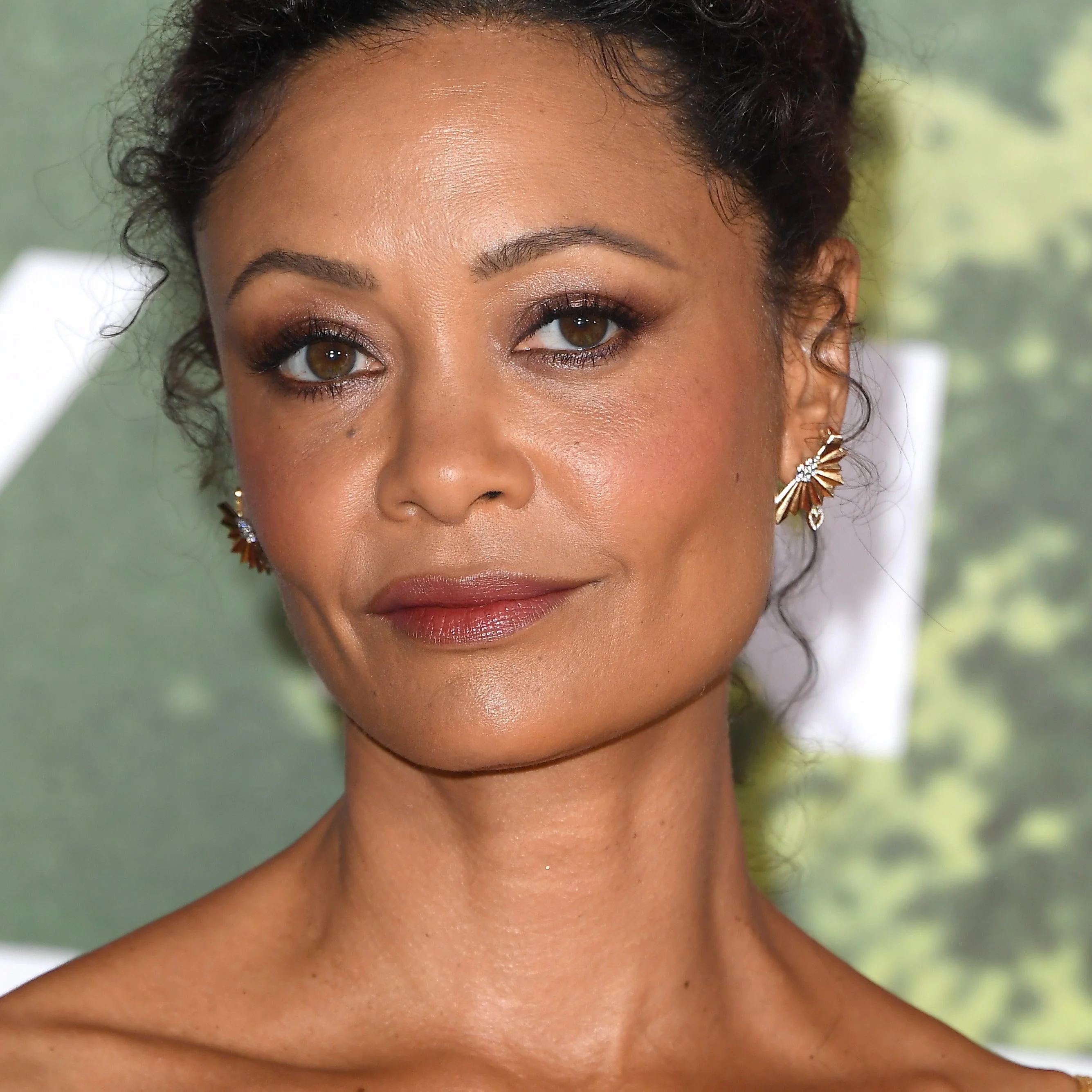 A person poses in an elegant updo hairstyle and decorative earrings at a formal event