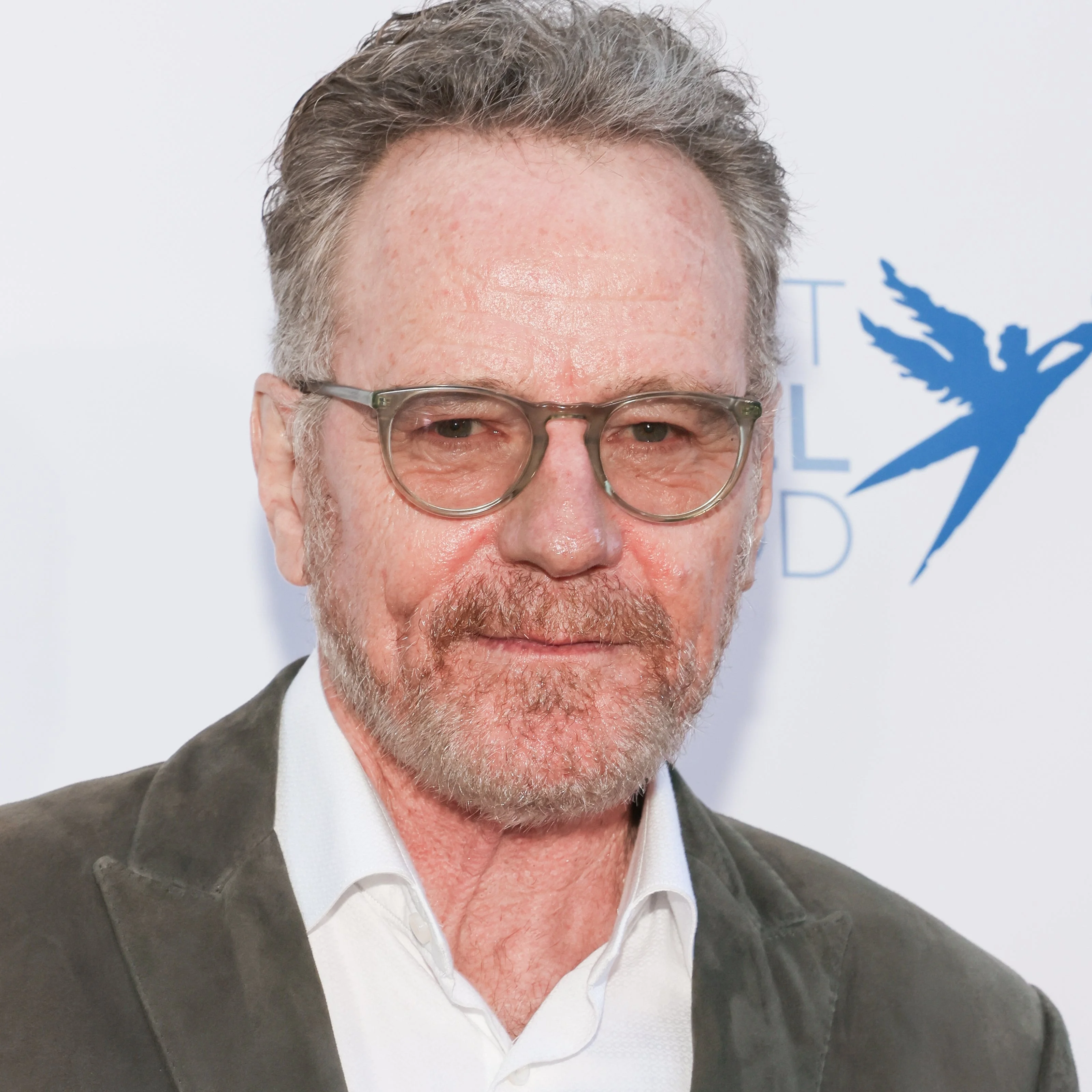 Man with glasses and a beard wearing a white shirt and gray suit jacket, smiling at an event