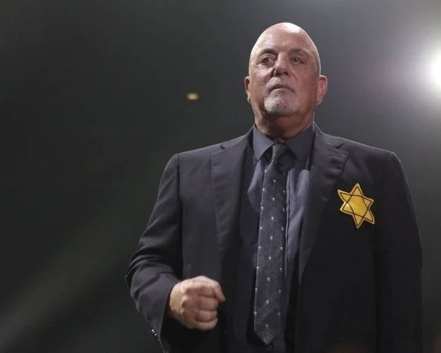 A man in a suit wears a yellow Star of David on his jacket during a performance