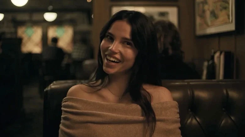 Inde Navarette as Nikki in Obsession, sitting in a restaurant booth and smiling.