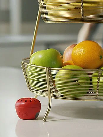 Small fly trap resembling an apple next to a large fruit stand.