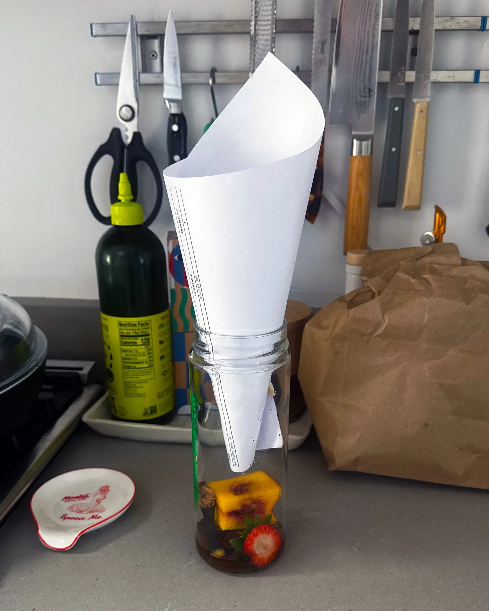 A fruit fly trap made out of a glass jar and paper funnel with cut strawberries and a peach pie