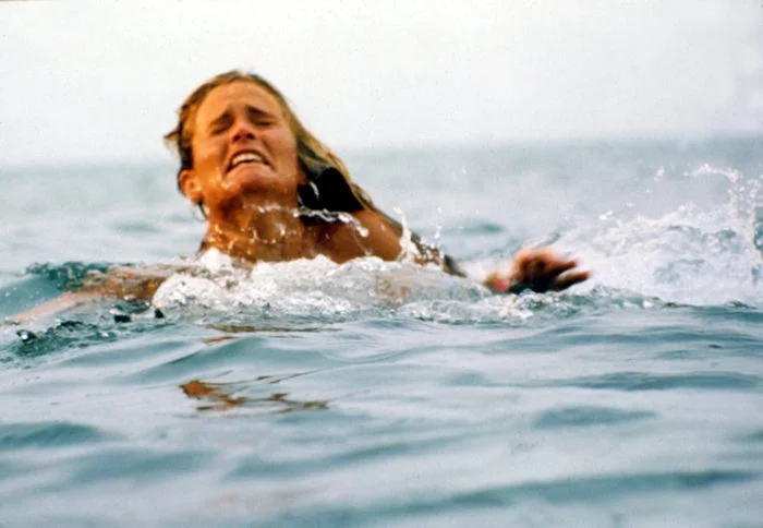 A person appears to be struggling while swimming in the ocean, displaying a distressed expression