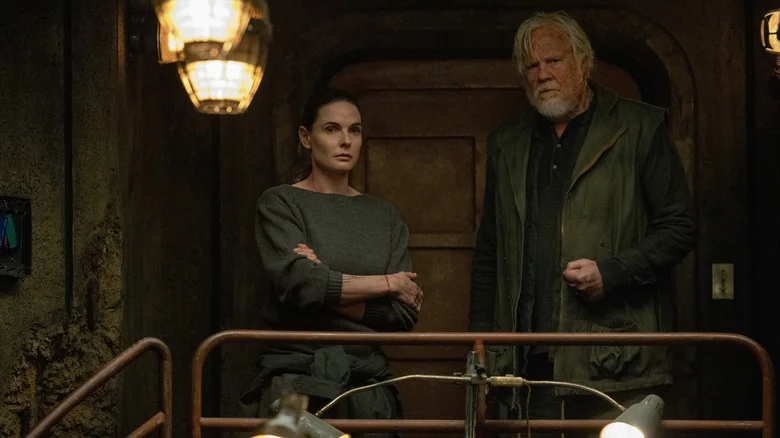 Rebecca Ferguson as Juliette Nichols standing next to Tim Robbins as Bernard Holland by a railing in Silo
