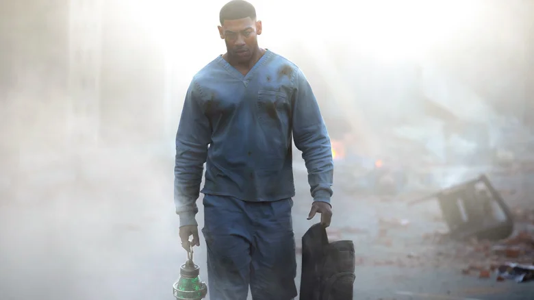 Aaron Pierre as John Stewart walking through a smoky street holding a backpack and lantern in Lanterns