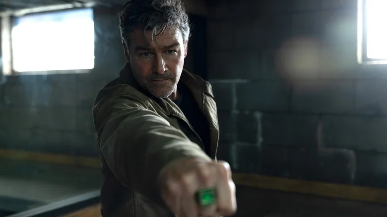 Kyle Chandler as Hal Jordan holding out his arm with a glowing green ring on his hand inside an interrogation room in Lanterns