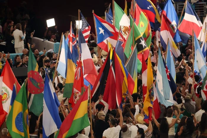 A diverse crowd waves numerous international flags at a large gathering, showcasing global unity and celebration