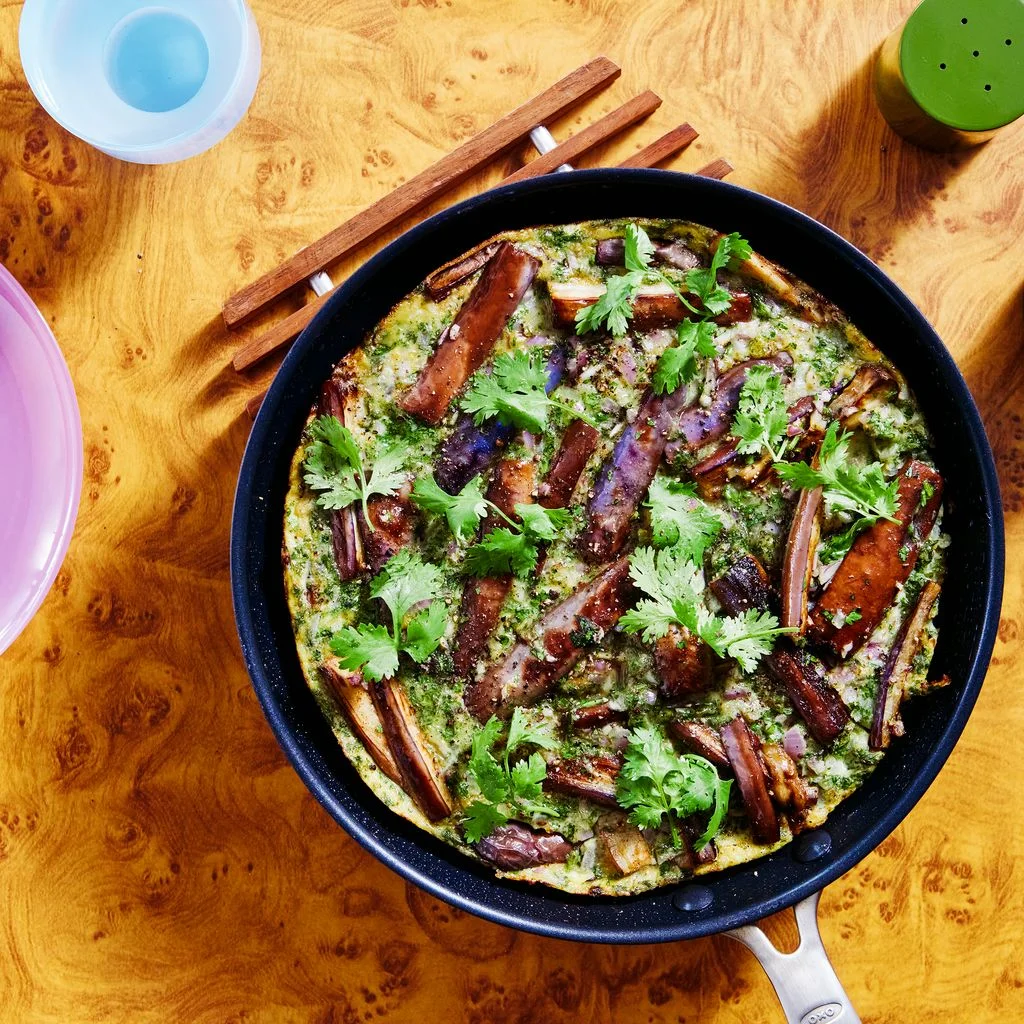 A colorful eggplant frittata in a frying pan with an equally colorful plate setting surrounding it.