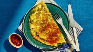 Spiced egg crepe folded over on a green plate with ketchup alongside