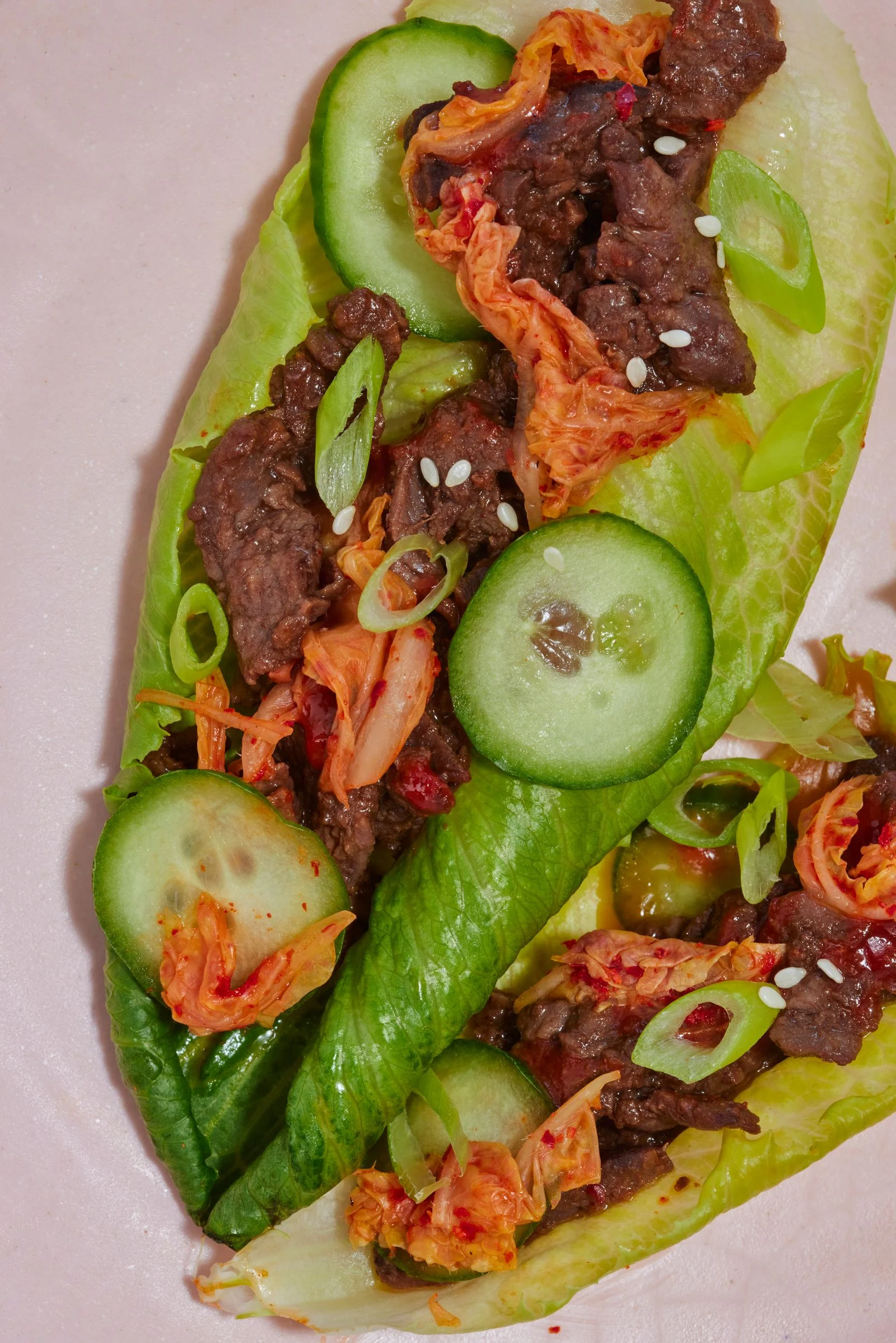 A lettuce wrap with beef bulgogi kimchi cucumbers and scallions.