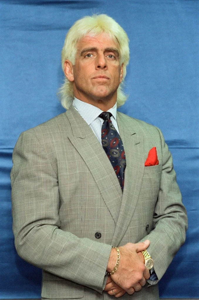 Person in a plaid suit with a striped shirt and patterned tie stands confidently against a blue backdrop, showcasing a classic professional style