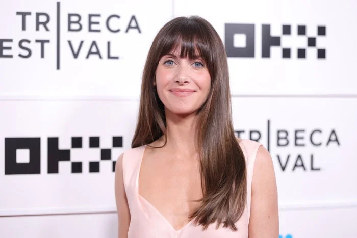 A person with long hair and bangs is wearing a sleeveless V-neck dress at a film festival event
