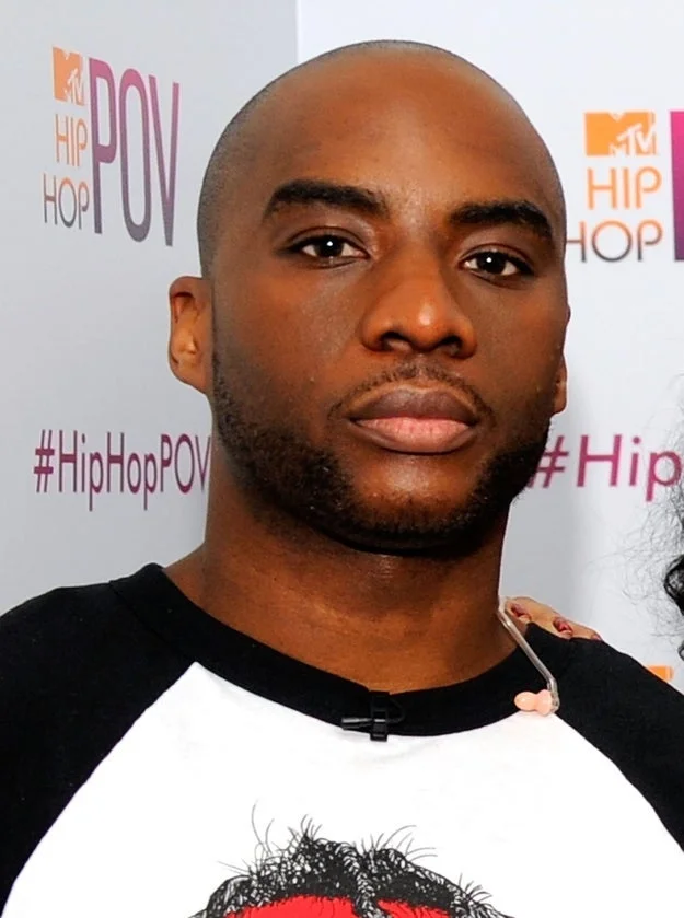 I don't know who this is. A person is standing in front of an MTV Hip Hop POV backdrop, wearing a casual t-shirt