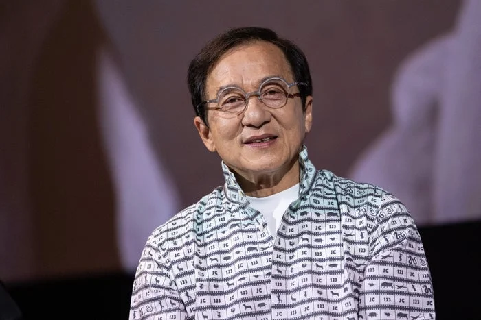 Person in glasses wearing a patterned shirt with a satisfied expression, attending an event