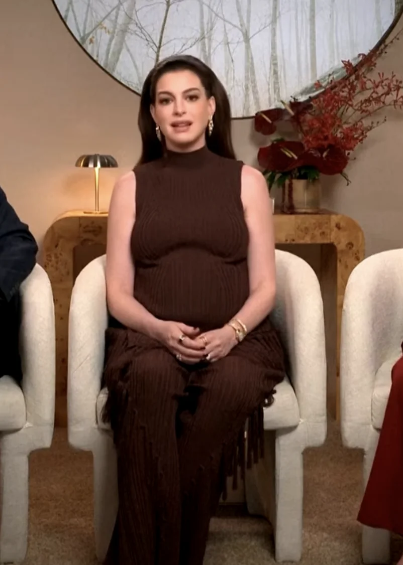 A person sitting in a chair, wearing a sleeveless, ribbed, long dress, with two people partially visible on the sides