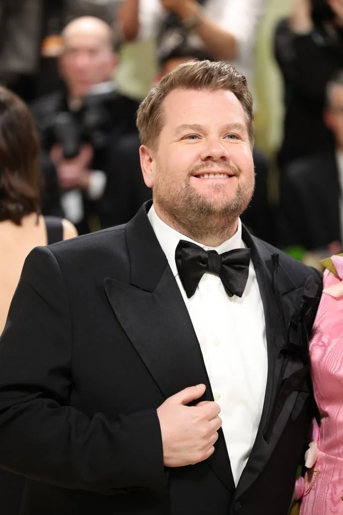 Person in formal black tuxedo smiles at an event, posing with others around in evening attire