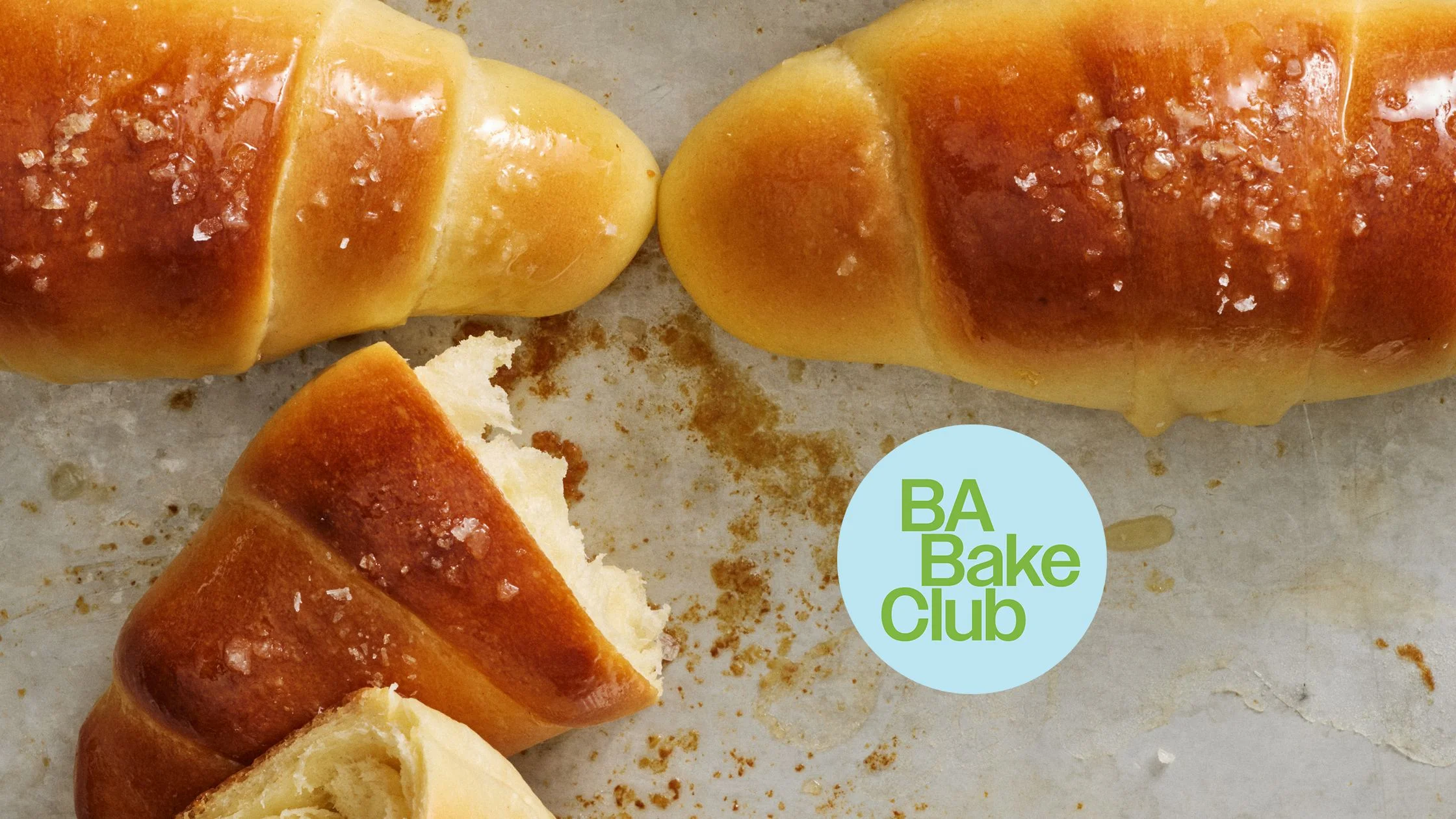 Salt Bread rolls fill a closeup of a baking sheet with browned tops coarse salt and one roll split open.