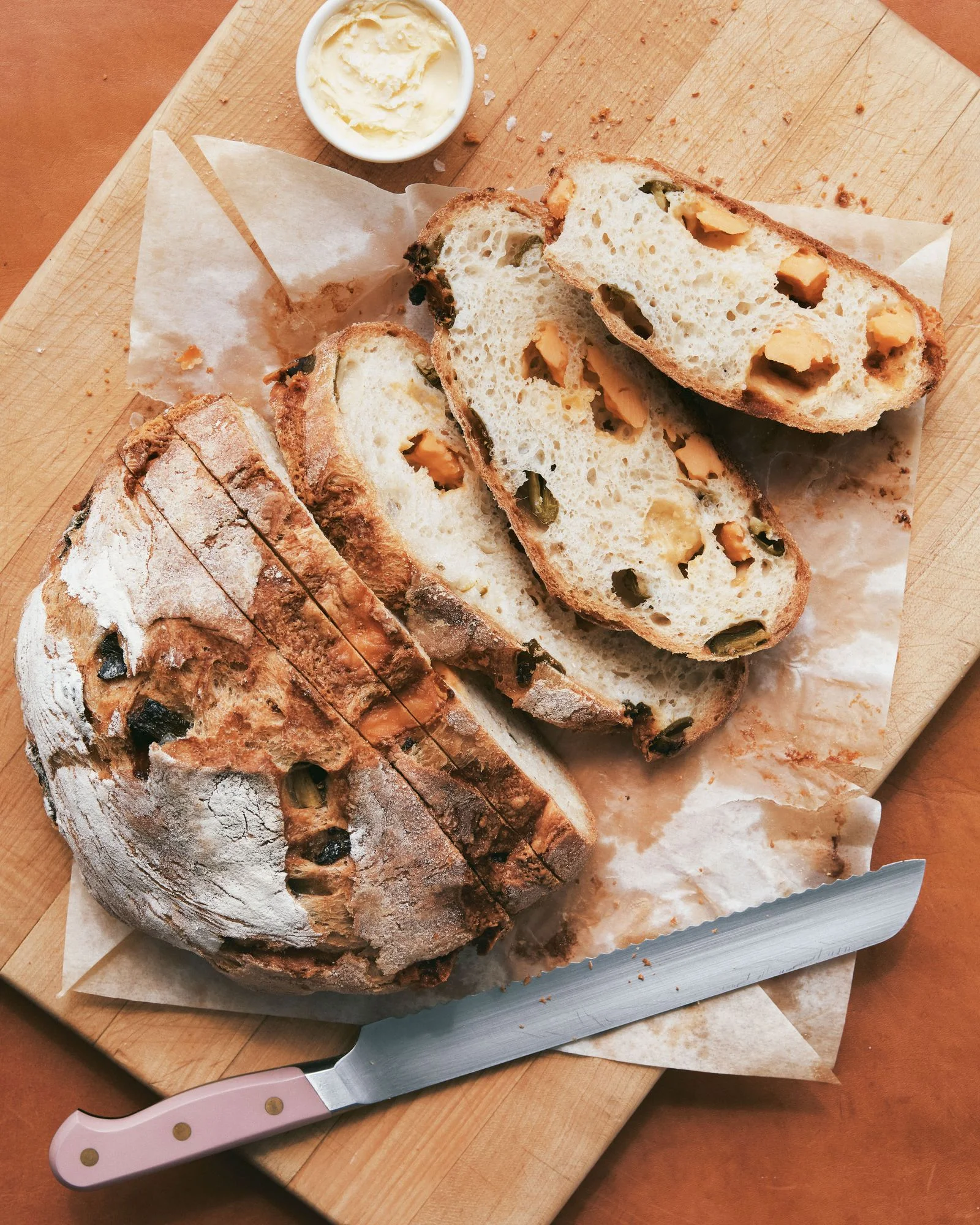 A sliced boule of cheddar jalapeño bread on a cutting board with butter and salt.