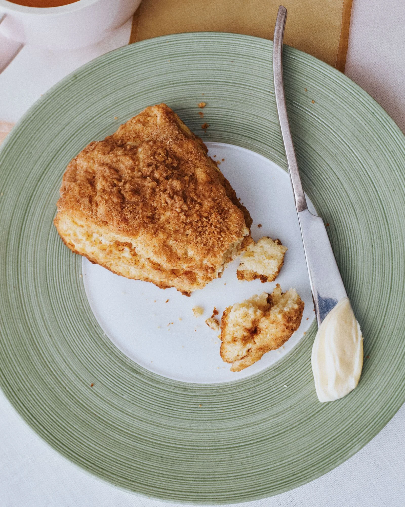 A coffee cake scone on a plate with a knife and butter..