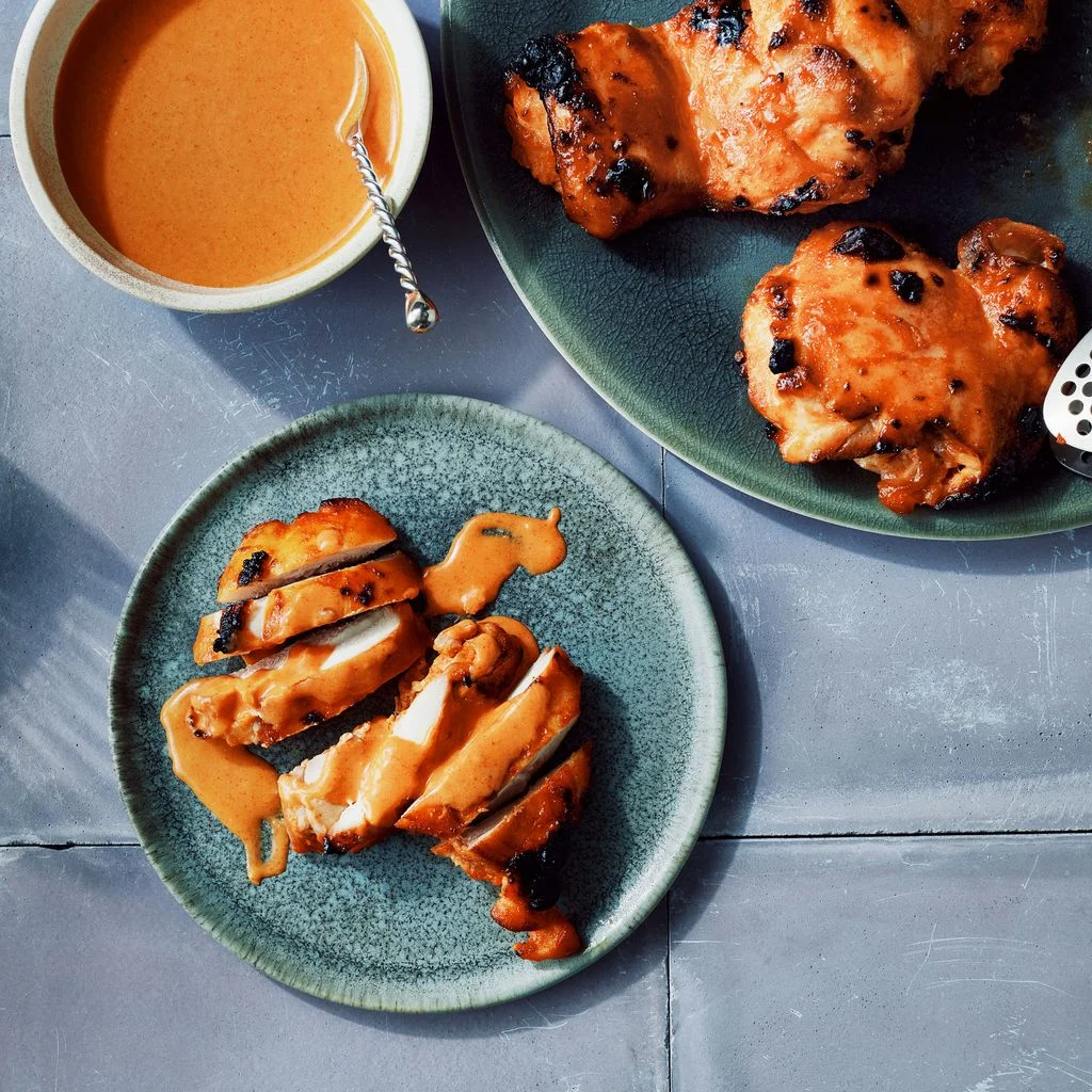 Gochujangyogurt marinated chicken thighs on a plate with a bowl of gochujangyogurt sauce and tongs.