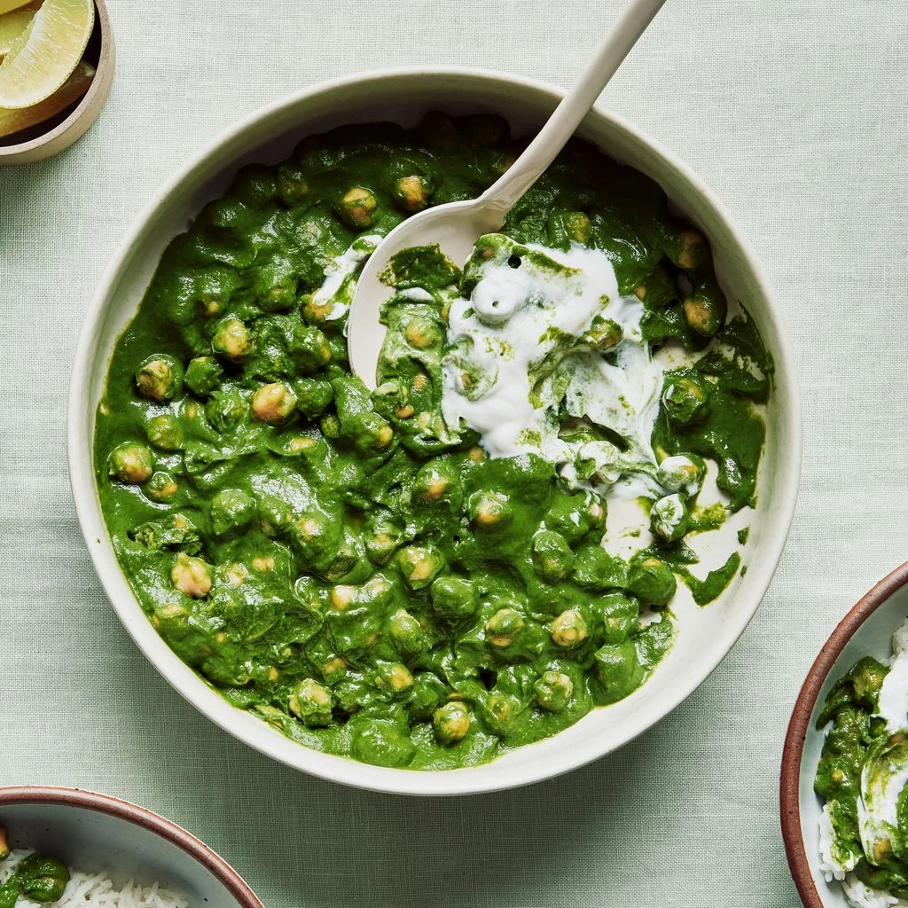 Pured spinach white onions ginger turmeric and Greek yogurt in a bowl with chickpeas and served with white rice and limes.