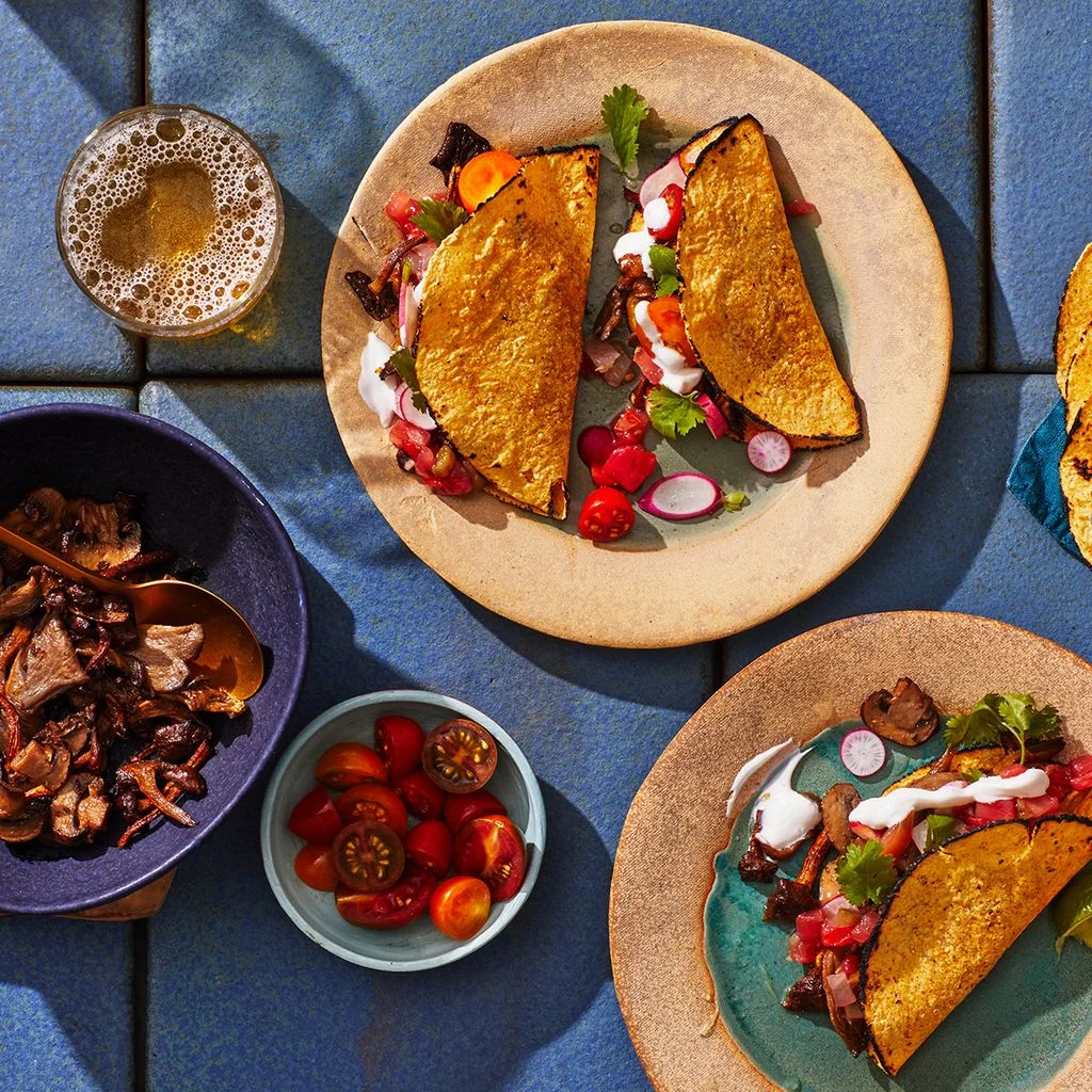 A spread of vegetarian spiced mushroom tacos with toppings including lime wedges cilantro charred tortillas and more.