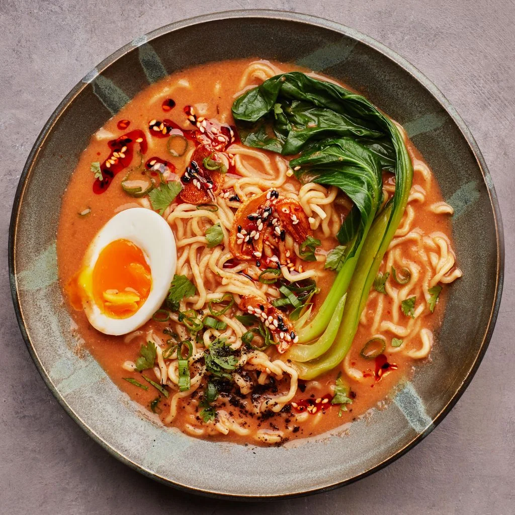 A bowl of vegetarian ramen with noodles bok choy a halved egg and chile garlic oil garnish.