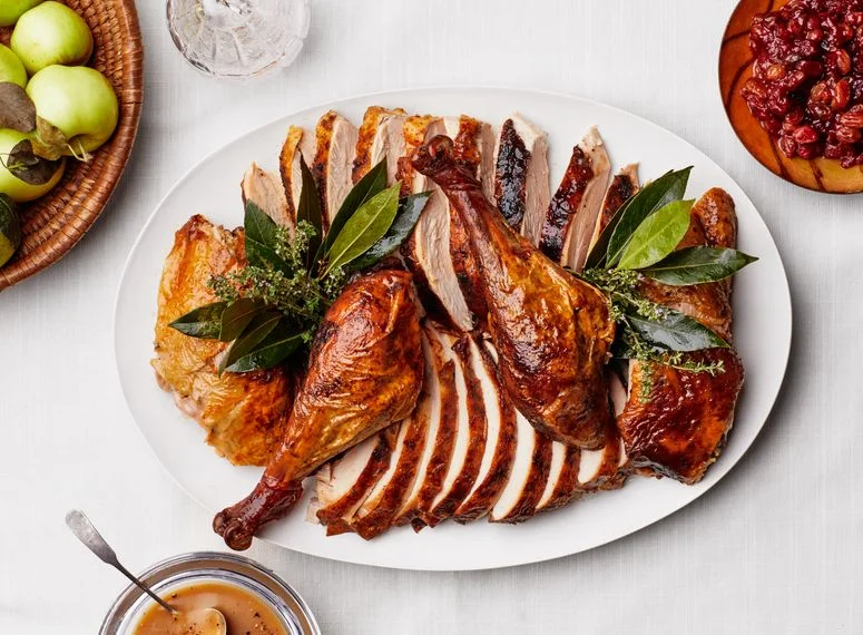 A carved turkey on a platter with neat slices of breast meat, whole drumsticks, and bundles of herbs tucked all around.