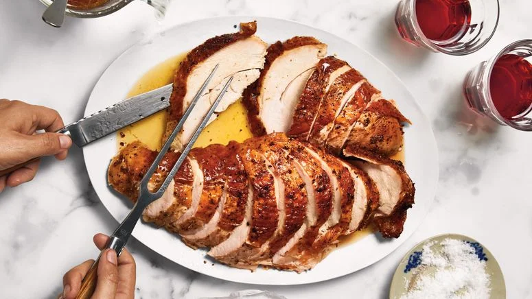 Two sliced turkey breasts on a platter being served with a slicing fork and knife.