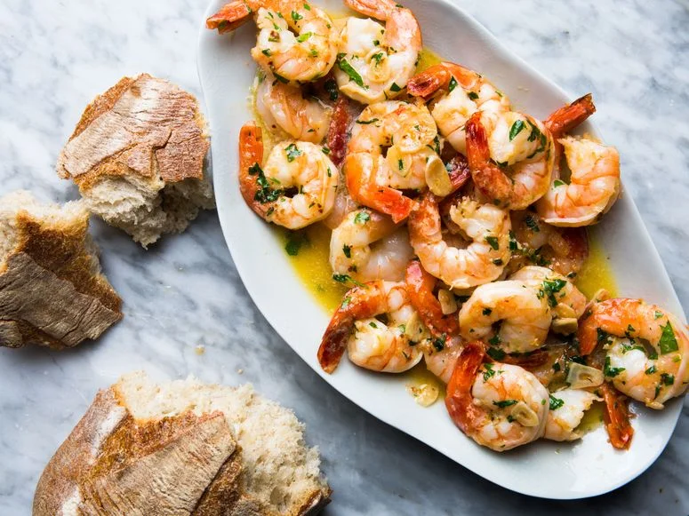 A pile of shrimp scampi on a platter with torn bread on the side for sopping.