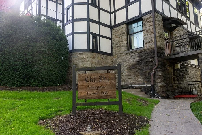 Sign in front of a Tudor-style building reads "Chi Psi, Craigielea, Founded 1869." Grass and a pathway are visible in the foreground