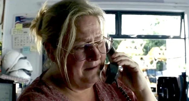 Person with glasses talking on the phone in an office setting, looking concerned
