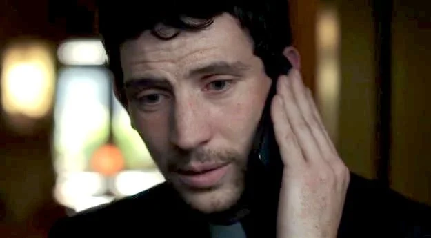 A person holding a phone to their ear, wearing a dark collared shirt, appears concerned