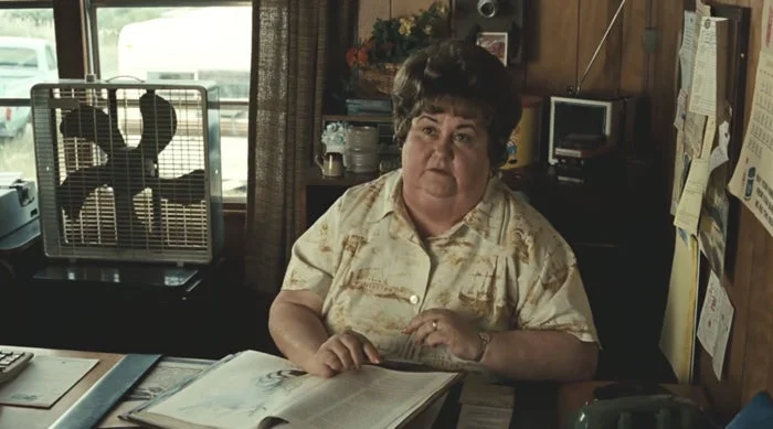 Kathy Lamkin sits at a desk with an open book, in a vintage-styled office. They appear thoughtful