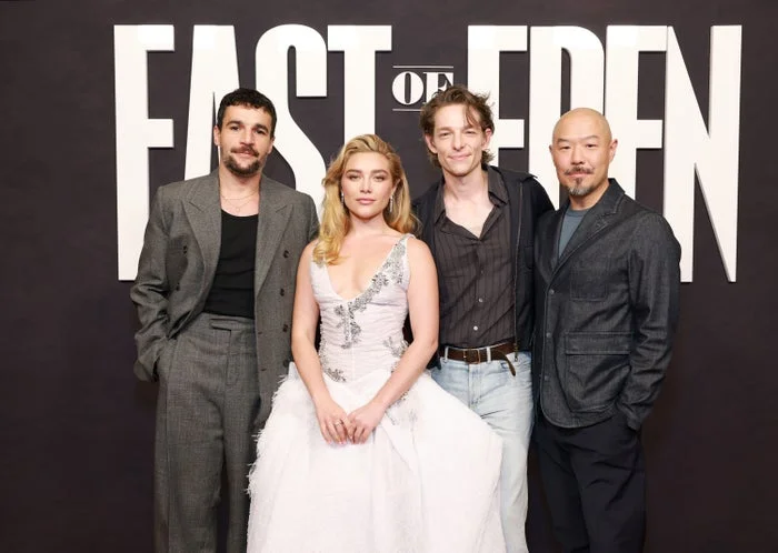 Four people in front of "East of Eden" sign; one in a white gown, others in smart casual outfits